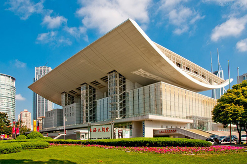 上海大剧院建筑设计由法国夏邦杰及华东建筑设计研究院中标;室内设计方案,由美国史迪奥和天舍文公司中标。总建筑面积为62803平方米,总高度为40米,分地下2层,地面6层,顶部2层,共计10层。其建筑风格新颖别致,融汇了东西方的文化韵味。白色弧形拱顶和具有光感的玻璃幕墙有机结合,在灯光的烘托下,宛如一个水晶般的宫殿。 图一 上海大剧院有近2000平方米的大堂作为观众的休闲区域,大堂的主要色调为白色,高雅而圣洁。大堂上空悬挂着由6片排箫灯架组合而成的大型水晶吊灯,地面采用举世罕见的希腊水晶白大理石,图案形似琴